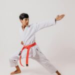 Teenage boy in martial arts pose wearing a white gi and red belt in studio setting.